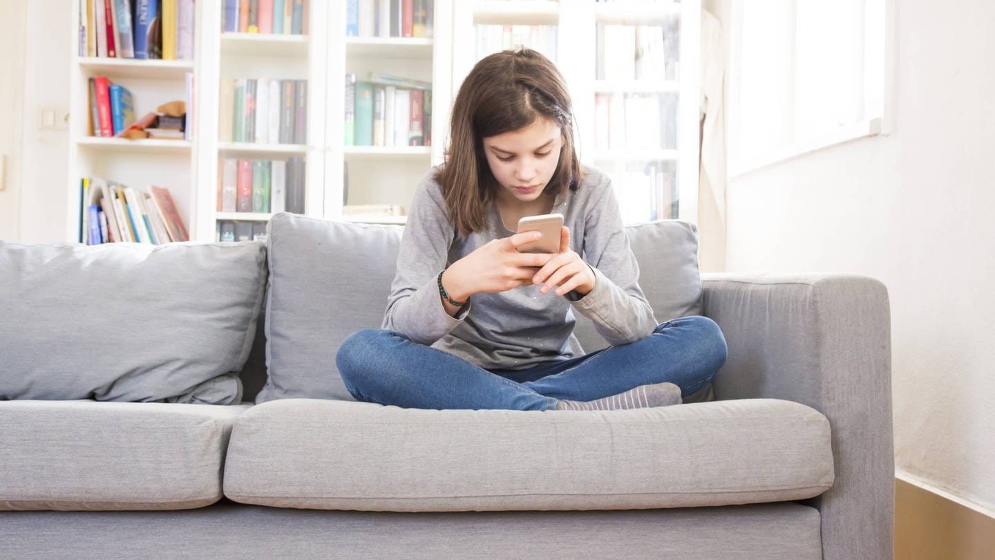 Mädchen sitzt mit Smartphone auf der Couch