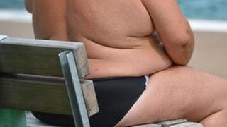 Ein übergewichtiger Mann sitzt auf einer Bank am Strand