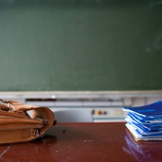 Klassenzimmer mit Aktentasche und Heftestapel vor einer Tagel: Vor allem Grund- und Förderschulen gehen die Lehrer aus. Es droht Unterrichtsausfall. Oft sind die Rektoren auf Quereinsteiger angewiesen.