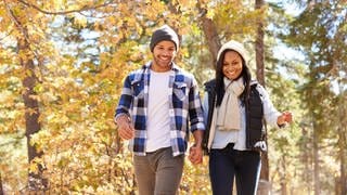 Ein junger Mann und eine junge Frau wandern lächelnd im Wald: Die Natur gibt uns Kraft. Immer häufiger zieht es Stadtmenschen raus ins Grüne. 