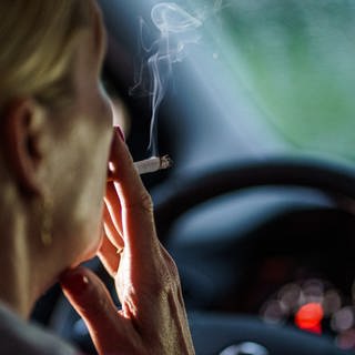 Eine Frau zieht hinter dem Lenkrad ihres Autos an einer Zigarette.