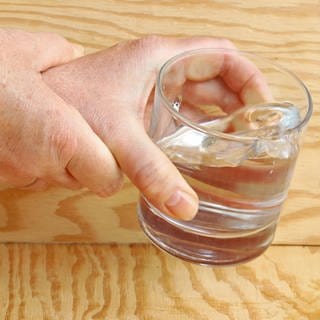 Zitternde Hände einer Parkinson-Patientin halten ein Wasserglas