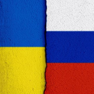 Nationalflaggen der Ukraine sowie von Russland im Anschnitt sowie einem Riss zwischen beiden Parteien.
