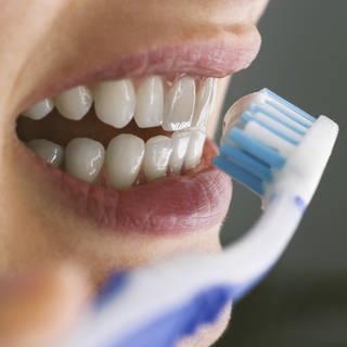 Eine Frau putzt sich die Zähne mit einer Handzahnbürste.