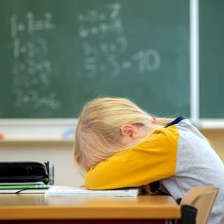Ein Schulkind liegt niedergeschlagen auf seiner Schulbank