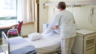 Eine Krankenpflegerin bereitet in einem Krankenzimmer ein Patientenbett vor.