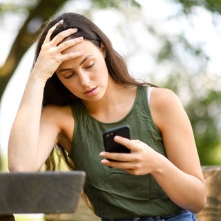 Eine junge Frau schaut verzweifelt auf ihr Smartphone.