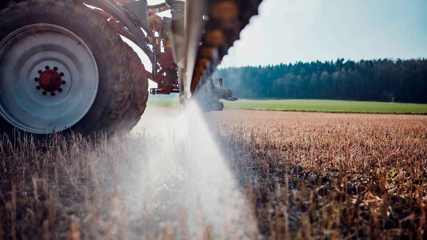 Nahaufnahme Teil eines Traktors, der über ein Feld fährt und Glykosphat spritzt.