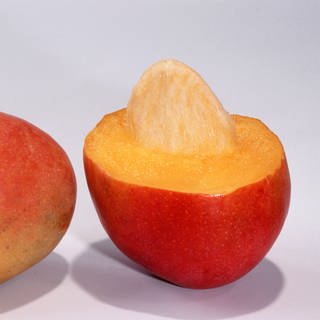 Eine ganze und halbe Mango-Frucht mit Kern.