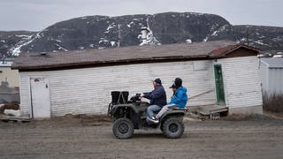 Kanada: Einheimische fahren an einem durch Erwärmung des Permafrostes, geneigten, schiefen Gebäude vorbei. 