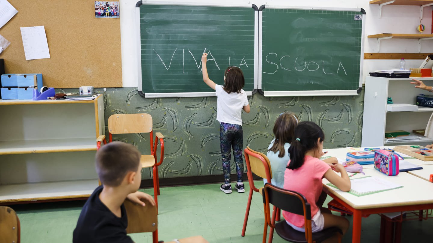 Klassenzimmer einer italienischen Grundschule. Ein kleines Mädchen schreibt auf die Tafel 
