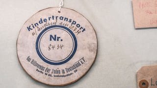 Anhänger an einem Teddybaer – Trostspender für eines der nach Großbritannien geretteten jüdischen Kinder, die 1938 und 1939 mit Kindertransporten verschickt worden waren. Bis 1939 kamen fast 10.000 Kinder nach Großbritannien. Viele sahen ihre Eltern nie wieder. – Exponat im Jüdischen Museum in Berlin. 