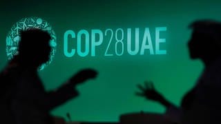 Zwei Menschen unterhalten sich vor einem Logo des UN-Klimagipfels COP28. 