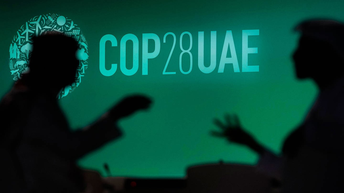 Zwei Menschen unterhalten sich vor einem Logo des UN-Klimagipfels COP28