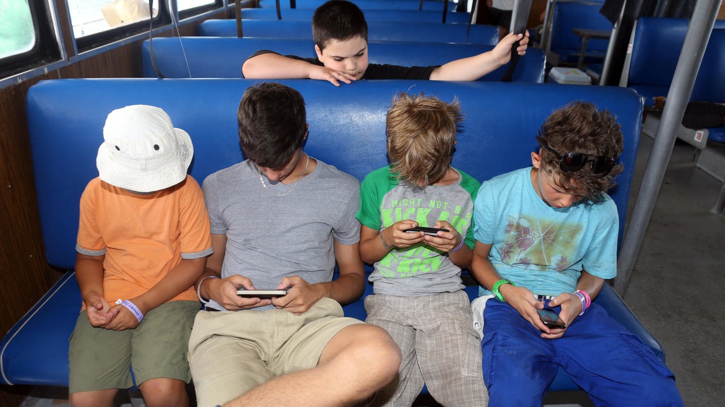 St. Pete Beach, Florida - Jungen schauen in einem Bus sitzend auf ihre Smartphones.