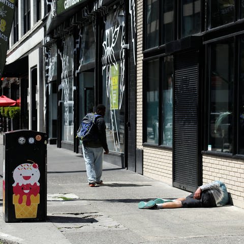 Mann liegt auf dem Fußweg ein Zweiter dreht sich nach ihm um, Ecke SW Broadway- SW Ankeny St, Downtown der Stadt Portland