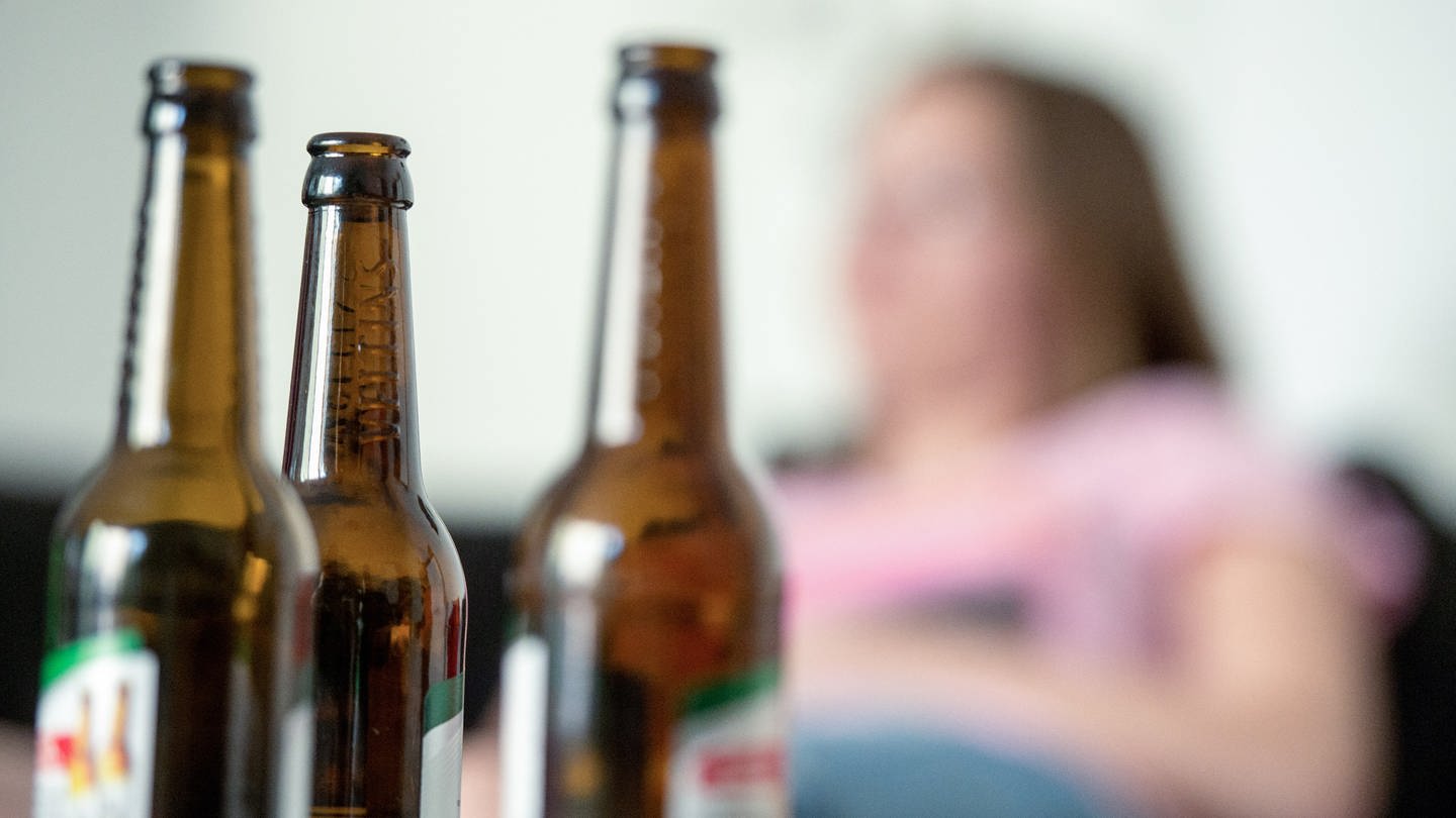 Eine junge Frau sitzt hinter leeren Bierflaschen. (zu dpa 