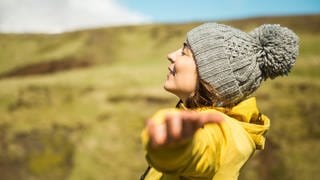 Junge Frau breitet in der Natur die Arme aus: Was ist Glück und wie können wir es finden?