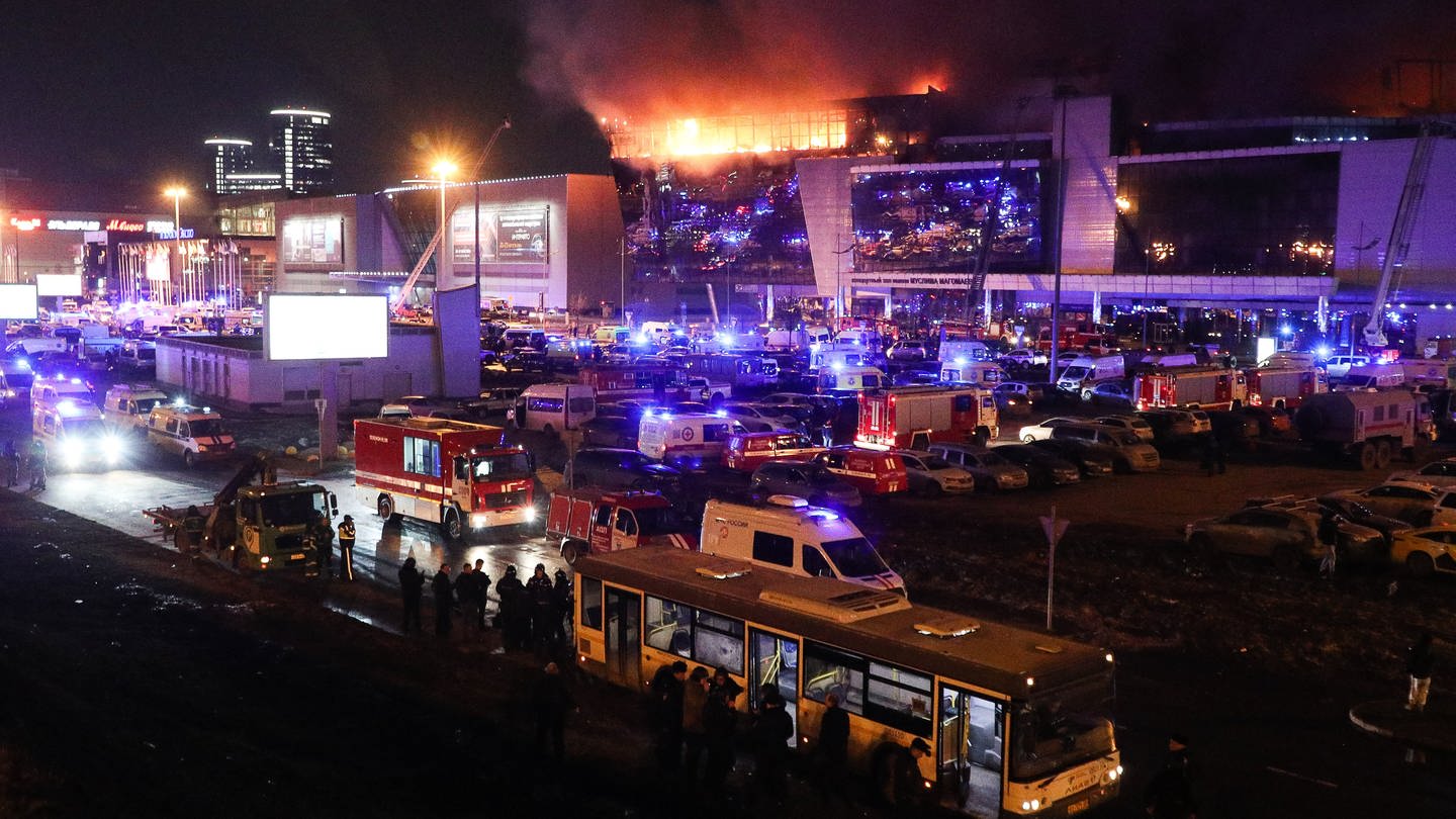 Nachts schlägt Feuer aus der Veranstaltungshalle Crocus City Hall, davor viele Feuerwehrfahrzeuge und Blaulicht: Beim Terroranschlag in Krasnogorsk bei Moskau am 22. März 2024 starben mindestens 144 Personen durch Schüsse und Feuer, 360 Menschen wurden verletzt. Die Terrorgruppe 