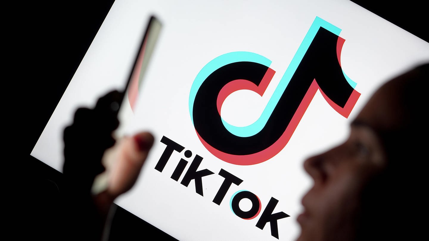 Silhouette einer Frau, die ein Smartphone hält, im Hintergrund das Logo der Videoplattform TikTok: Die Social-Media-Plattform TikTok ist schon lange Teil der Popkultur – mittlerweile zeigt sich aber auch der politische Einfluss der App. Denn neben Influencern tummeln sich hier auch Parteien, Politiker und Aktivisten.