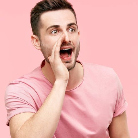 Mann im rosa T-Shirt hält rechte Hand an den Mund und ruft: Die menschliche Stimme ist einzigartig wie ein Fingerabdruck. Studien belegen, dass wir durch den Klang der Stimme Rückschlüsse auf Kompetenz, Attraktivität und Alter einer Person ziehen. 