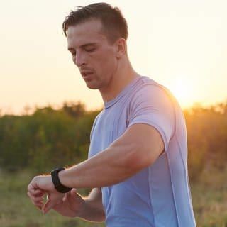 Inmitten der sonnigen Atmosphäre blickt ein Sportler beim Laufen auf seine Smartwatch.