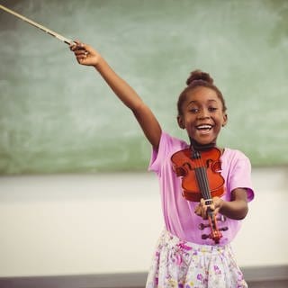 Porträt einer lächelnden Schülerin, die im Klassenzimmer Geige spielt.
