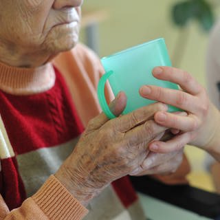 Eine Pflegekraft hilft einer alten Frau in einem Seniorenheim beim Trinken aus einem Beche