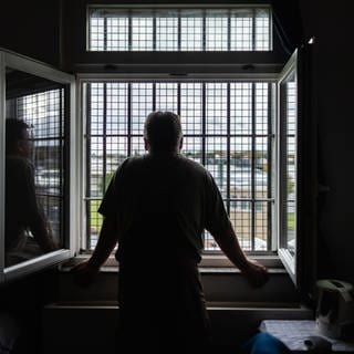 Ein älterer Häftling schaut durch das vergitterte Fenster seiner Zelle: Häftlinge kämpfen mit Süchten, Depressionen, Schuldgefühlen, Ängsten oder Psychosen. Die Suizidrate ist deutlich höher als bei Menschen außerhalb des Strafvollzugs.