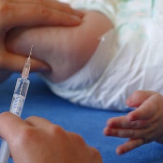 Säugling beim Kinderarzt: Setzen einer Spritze durch die Kinderärztin in den Oberschenkel des Kindes.