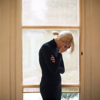 Traurige blonde Frau vor großen Fenstern