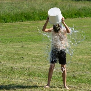 Symbolbild: Teenager schüttet sich im Freien einen Eimer kaltes Wasser über den Kopf. 