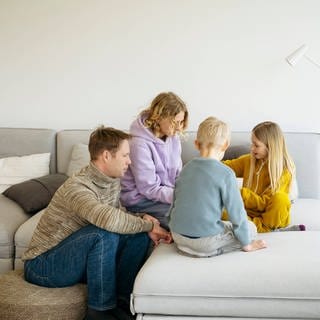 Eltern mit Kindern, die zu Hause gemeinsam auf dem Sofa spielen (Symbolfoto)