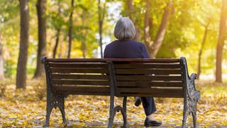Ältere Frau sitz in einem Herbstwald einsam auf einer Bank: Einsamkeit ist ein wachsendes gesellschaftliches Problem. Unterschiedliche Projekte sollen einsamen Menschen helfen