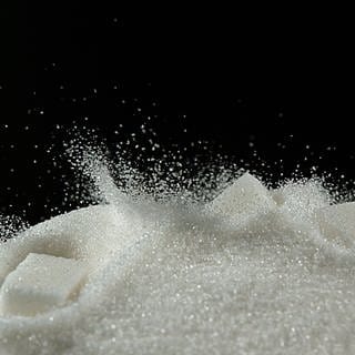 Weißer Zuckerwürfel fällt auf Puderzucker vor schwarzem Hintergrund