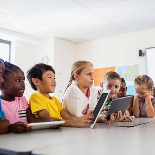 Eine Lehrerin sitzt mit Grundschulkindern an einem Tisch