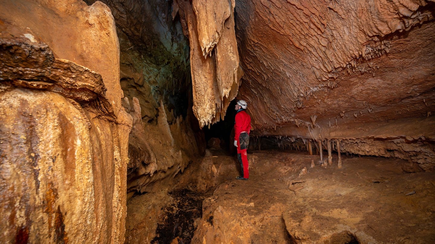 A speleologist with helmet and headlamp exploring a cave with rich stalactite and stalagmite formations. Symbolfoto