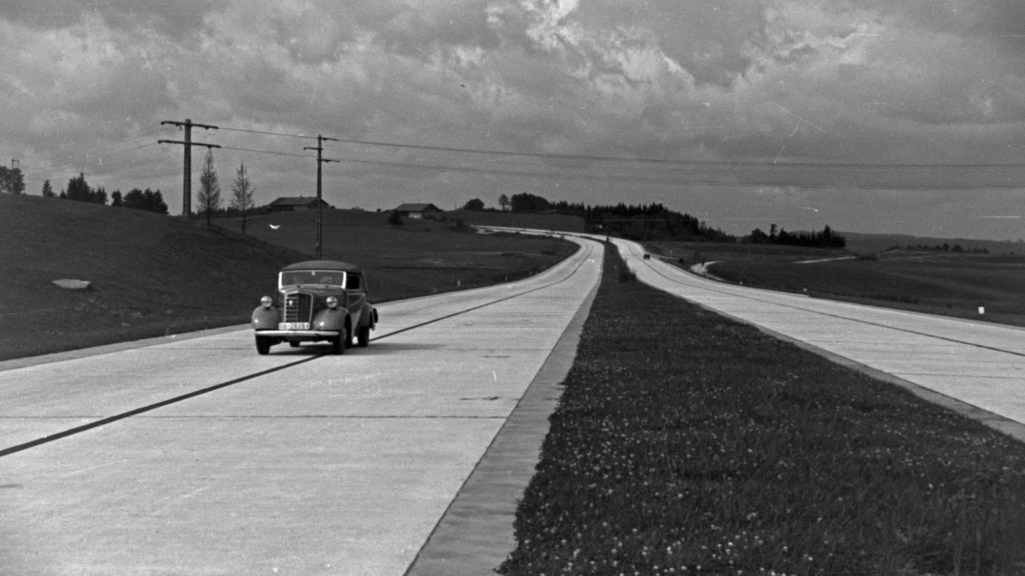 In den 1930ern unterwegs auf der Reichsautobahn: ein einsamer PKW: Mit der Möglichkeit, große Entfernungen schnell zu überwinden, spielen Autobahnen bis heute eine wichtige Rolle für die infrastrukturelle und wirtschaftliche Entwicklung. Doch mit dem steigenden Bewusstsein für Umwelt- und Klimaschutz gerät eine Verkehrspolitik, die auf Autobahnen und Individualverkehr setzt, zunehmend in die Kritik.