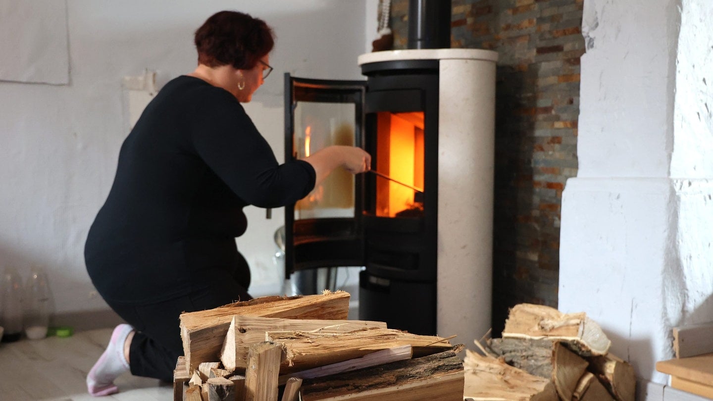 Eine Frau feuert im Wohnzimmer ihren mit Holz an: Um sich gegen die Gaskrise zu wappnen, haben in Deutschland viele Menschen Kaminöfen und Holz jeder Qualität gekauft. Allerdings: Im Winter droht vor allem bei Inversionswetterlagen eine Feinstaubbelastung, die alle Grenzwerte sprengen könnte. Asthmatiker verzweifeln, stoßen bei den Behörden jedoch auf Achselzucken.