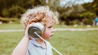 Ein kleiner Junge hält sich die Dose eines Schnurtelefons ans Ohr. Forschende sind sich einig: Zum richtigen Zuhören gehört kognitive Aufmerksamkeit mindestens genauso sehr wie die akustische Schallaufnahme. 