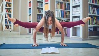 Ein Frau liest ein Buch, während sie im Handstand eine Yoga-Übung macht: Kognitionsforscher haben klar nachgewiesen, dass durch Bewegung die Bildung von Strukturen im Gehirn stimuliert wird. Und das gilt für jedes Lebensalter: Während den Jüngeren die Bewegung hilft, Wissen aufzubauen, unterstützt sie Ältere, Dinge im Gedächtnis zu behalten.