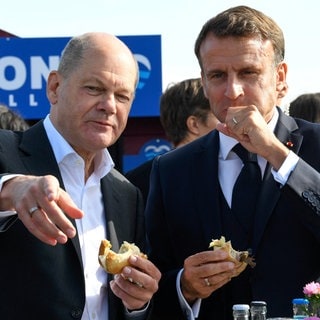 Bundeskanzler Olaf Scholz (SPD) und Frankreichs Präsident Emmanuel Macron (rechts) essen gemeinsam in Blankenese an der Elbe ein Fischbrötchen. Das deutsche und das französische Kabinett trafen sich im Oktober 2023 in der Hansestadt zu einer zweitägigen Klausur. Gemeinsames Speisen ist eines der ältesten Instrumente der Diplomatie, um Verständigung und Kooperation zu fördern. Macron schien nicht ganz so begeistert von der norddeutschen Spezialität.