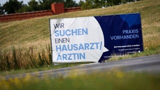 Ein Plakat mit dem Text "Wir suchen einen Hausarzt  Ärztin - Praxis Vorhanden" steht am Ortseingang von Friederichskoog. Hausärzte werden in vielen ländlichen Regionen gesucht.