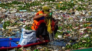 Ein Mann in einem Boot versucht den Citarum-Fluss auf Java in Indonesien von Plastik zu reinigen. Sein kleines Boot ist von Abfall dicht umschlossen.