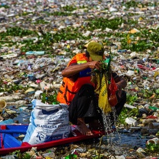 Ein Mann in einem Boot versucht den Citarum-Fluss auf Java in Indonesien von Plastik zu reinigen. Sein kleines Boot ist von Abfall dicht umschlossen.