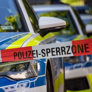 Rot-weißes Absperrband mit der Aufschrift "Polizei-Sperrzone", dahiner Polizeiautos: Die Anzahl psychisch erkrankter Menschen in Deutschland steigt seit Jahren. Auch die psychischen Krisen nehmen zu. Kommt es deswegen zu einem Polizeieinsatz, kann das für Betroffene gefährlich sein, denn nicht selten enden solche Situationen tödlich. 