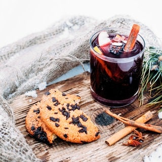 Ein Glas Glühwein auf einem Holzbrett auf einem verschneiten Tisch mit Keksen mit geriebener Schokolade