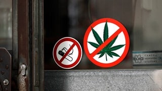 Zwei Aufkleber an der Eingangstür eines Restaurants zeigen, das Rauchen und der Konsum von Cannabis im Restaurant verboten sind: Ein Blick in die 200-jährige Geschichte der Drogenprohibition zeigt: Die Entscheidung, ob eine berauschende Substanz legal oder illegal ist, wurde recht willkürlich gefällt. Sie hatte wenig mit Gesundheitsschutz zu tun, dafür aber viel mit Rassismus, Diskriminierung und Stigmatisierung.