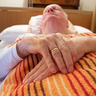 Ein alter Mann liegt im Bett: Wenn die Schmerzen unerträglich werden und keine Aussicht auf Besserung besteht, entscheiden sich manche Menschen dafür, auf Essen und Trinken zu verzichten. Das "Sterbefasten" gilt als eine eher natürliche Form des Sterbens, da Sterbende in ihrer letzten Lebensphase ohnehin weniger bzw. gar keine Nahrung mehr zu sich nehmen.