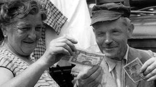 Ein Ehepaar vergleicht am 6. Juli 1959 auf dem Saarbrücker Markt alte und neue Geldscheine